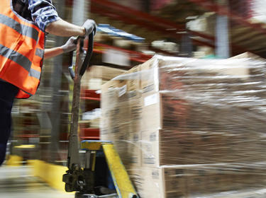 Worker pushing a pallet jack loaded with inventory inside a warehouse