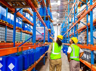 Two people walking in a warehouse in safety vests and hard hats