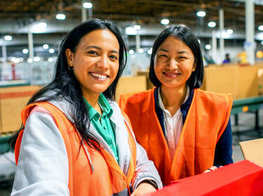 Due donne che sorridono in un magazzino in abiti arancioni Due donne che sorridono in un magazzino in abiti arancioni